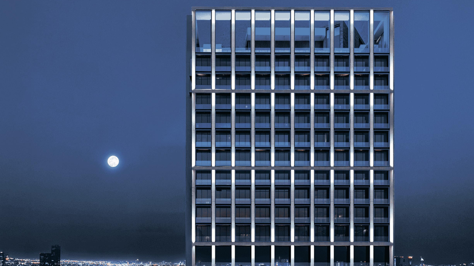 Modern high-rise building illuminated under a moonlit sky with panoramic city views
