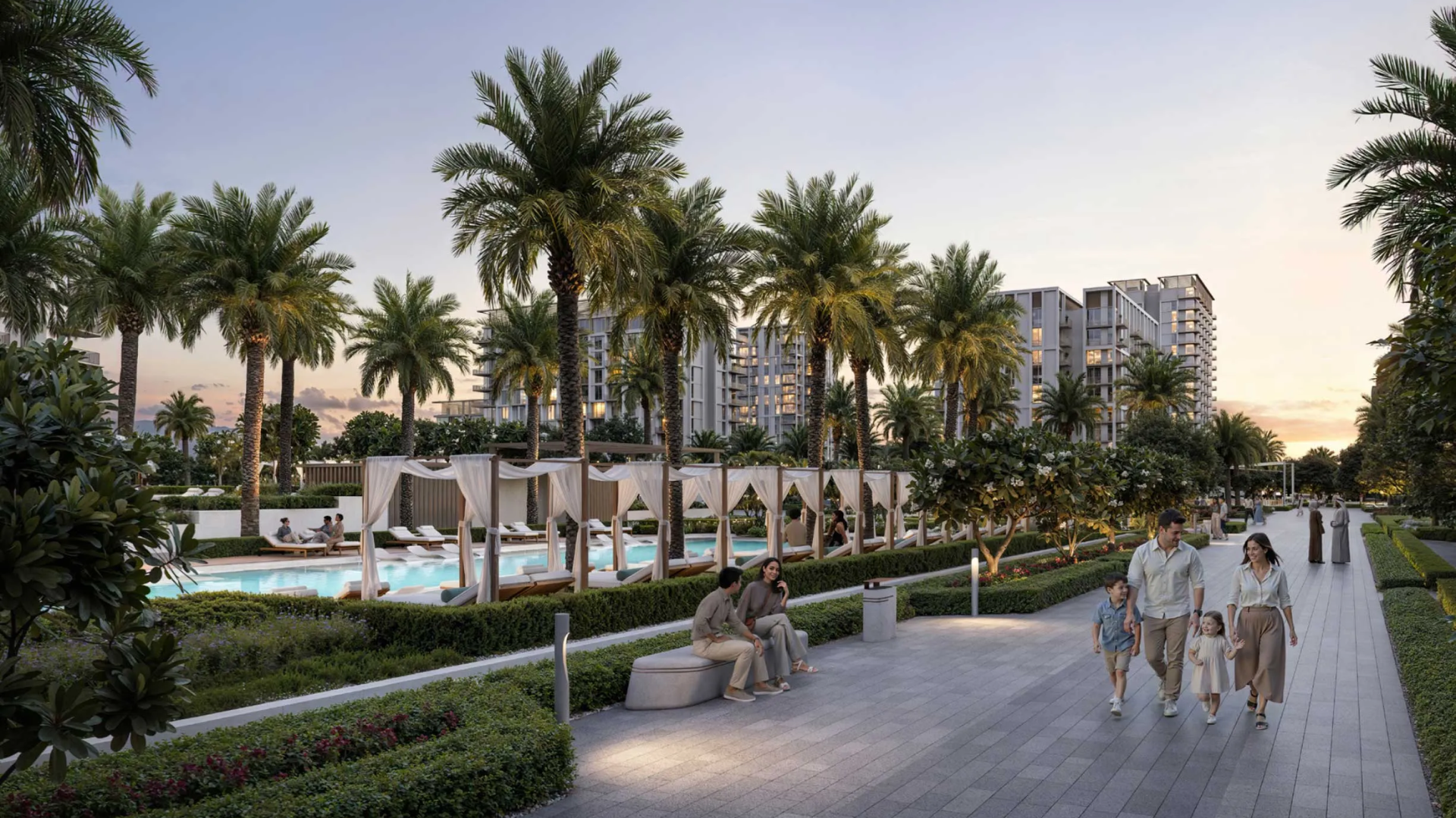Evening view of a landscaped walkway with families strolling, poolside cabanas, palm trees, and modern residential buildings.
