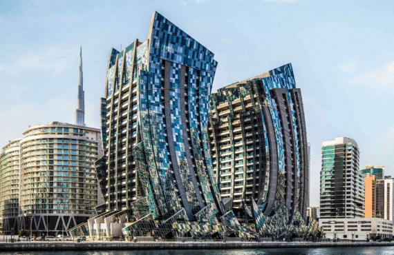 Modern architectural towers with fragmented glass facades overlooking a canal, with the Burj Khalifa in the background.