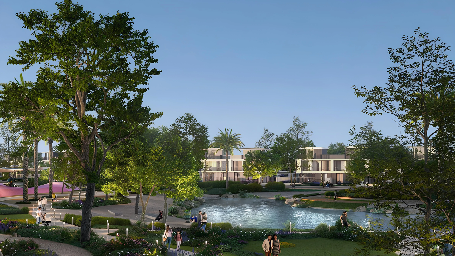 Residential community park featuring a pond, walking paths, mature trees, and modern townhouses in the background.