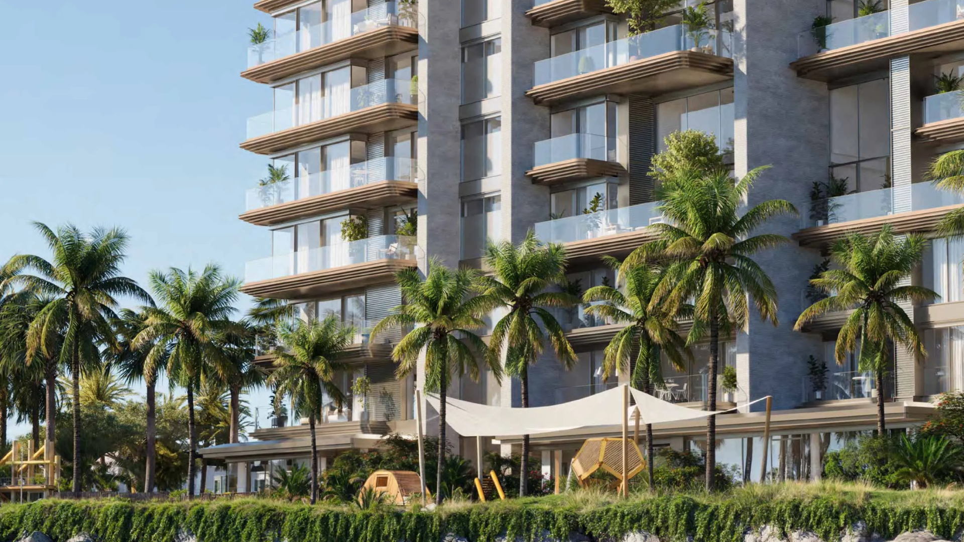 A modern residential building exterior with glass balconies, palm trees, and a shaded outdoor children's play area.
