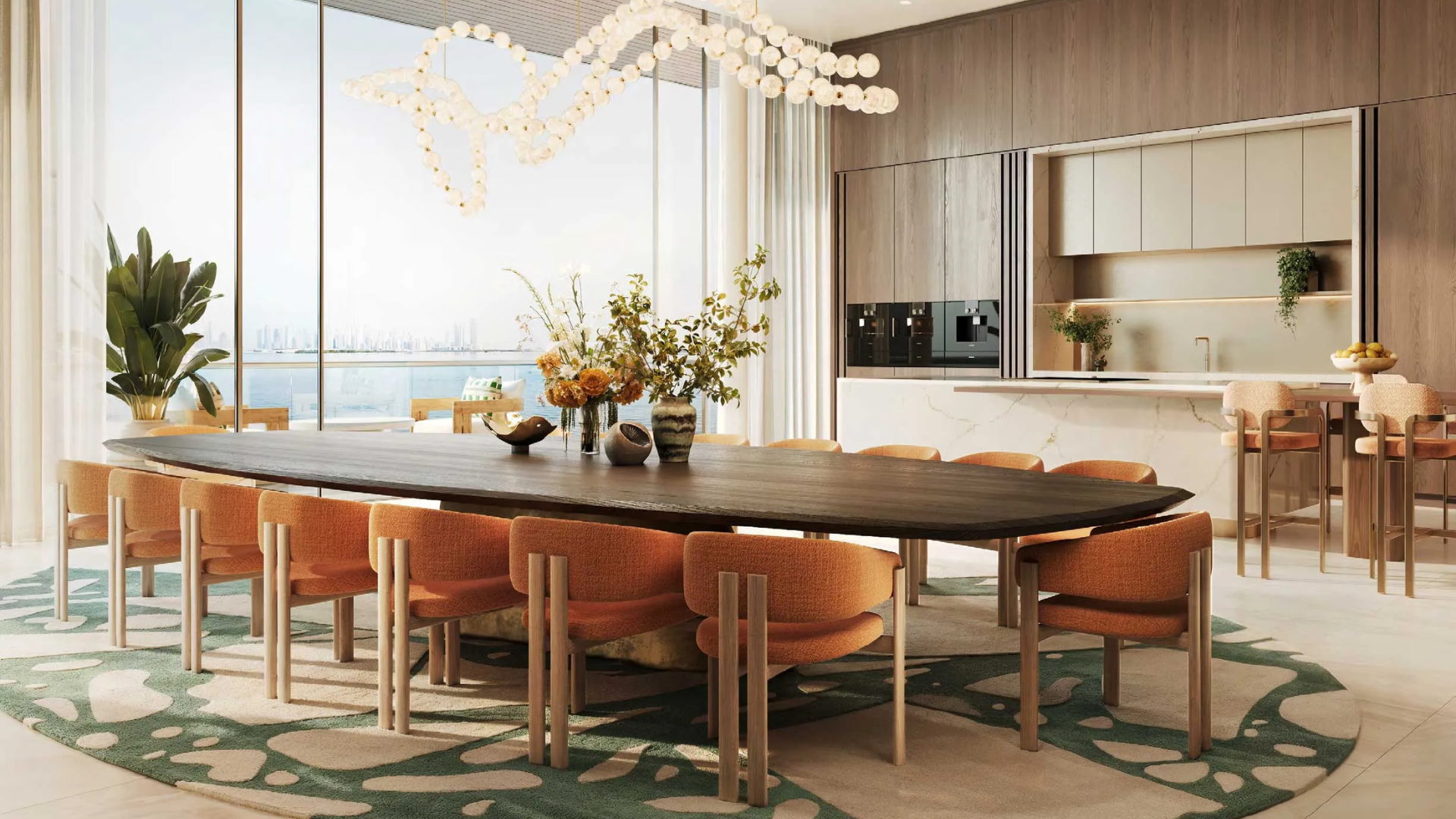 Luxury open-plan dining and kitchen area with a large oval table, orange chairs, and a panoramic sea view.