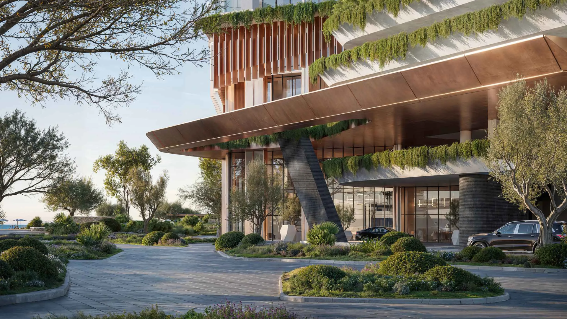 Modern building entrance with cantilevered canopy, greenery cascading from terraces, landscaped driveway, and parked cars.